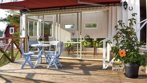 Ein überdachter Außenbereich mit Tisch und Stühlen, einem Blumentopf und Blick auf das Haus durch Glastüren.