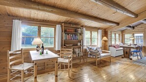 Un accogliente interno di una baita con pareti in legno, un tavolo da pranzo con sedie, una libreria e un angolo cottura.