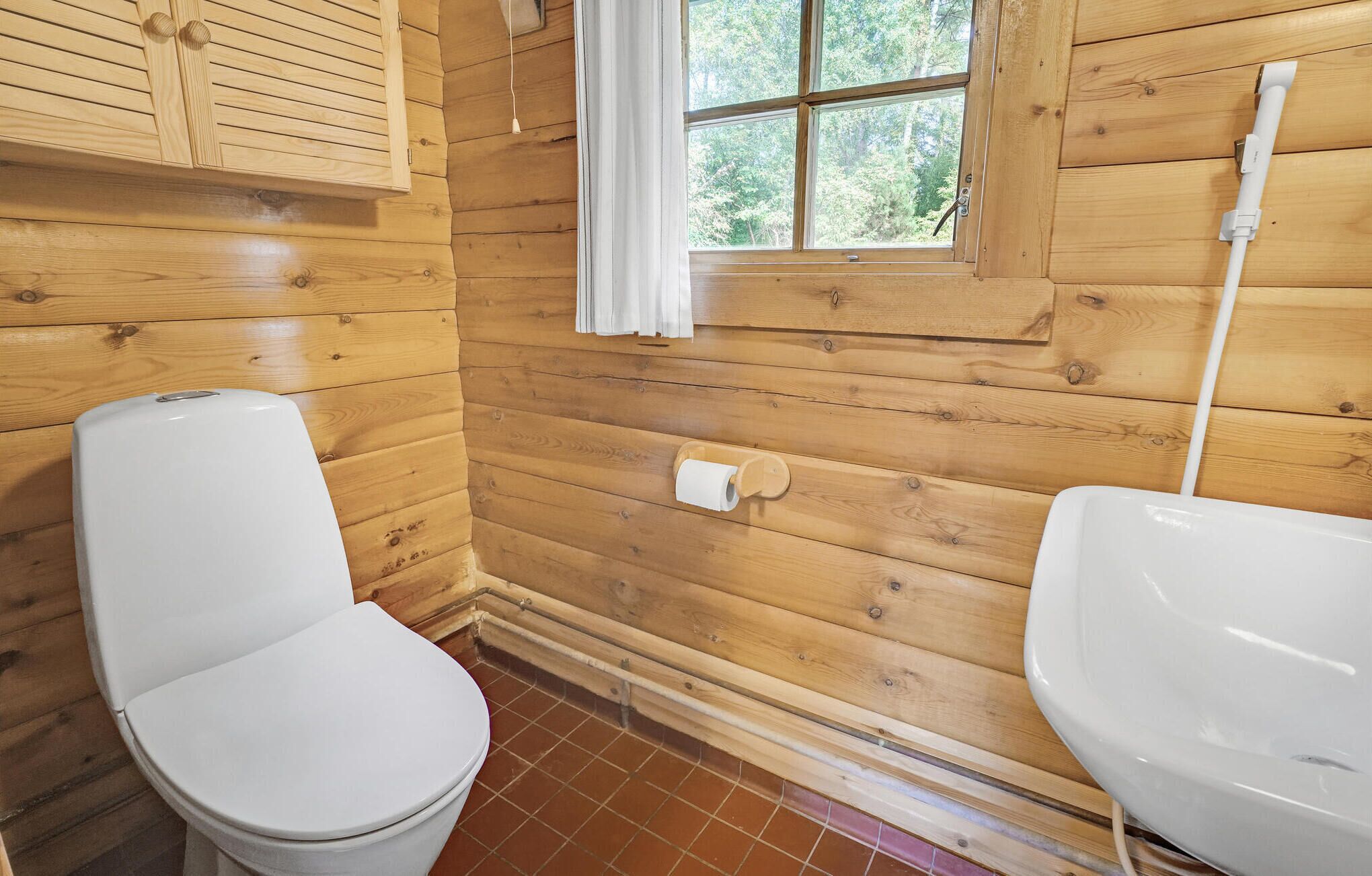 A wooden cabin bathroom with a toilet, sink, and window.
