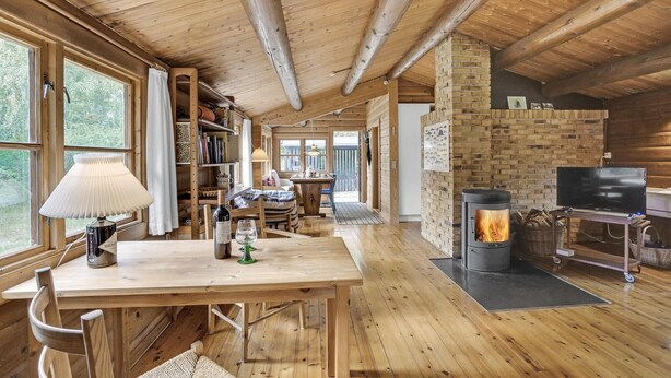 Un accogliente interno di una baita con un tavolo da pranzo in legno, librerie, un camino e un televisore.