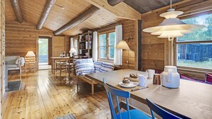 Un accogliente interno di una baita con un tavolo da pranzo in legno, sedie blu, una panca e una libreria.