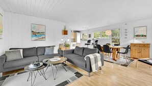 Una sala de estar moderna con un sofá seccional gris, una mesa redonda de centro y un comedor con una mesa y sillas de madera.