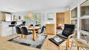 Un interior moderno con comedor, una zona de estar con sofá y una cocina visible a través de una puerta abierta.