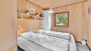 Un dormitorio con paredes de madera, una ventana, una cama y una estantería con libros y una planta.