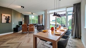 A modern dining area with a long wooden table, black chairs, and a view of the outdoors through large windows. - Nice home in Vlagtwedde (Vlagtwedde)