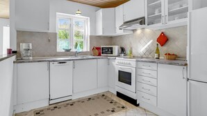 A modern kitchen with white cabinets, a built-in microwave, a stove, and a window with a view of greenery. - 3 bedroom nice home in Læsø (Læsø)