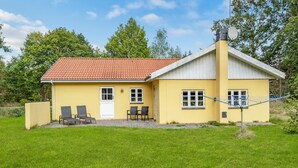 A yellow building with a red-tiled roof, two windows, and a door. There are four chairs outside. - 3 bedroom nice home in Læsø (Læsø)