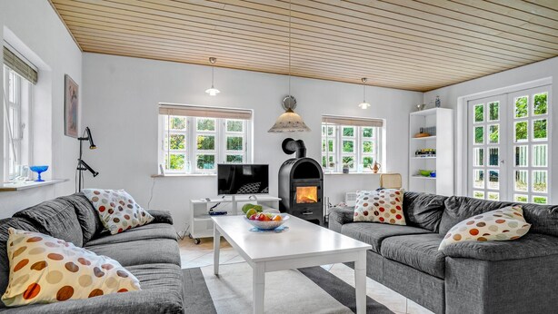 A modern living room with two grey sofas, a white coffee table, a black wood-burning stove, and large windows with white frames. - 3 bedroom nice home in Læsø (Læsø)