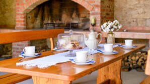 A wooden table set with white cups and saucers, a glass cloche, and a white pitcher, with a brick fireplace in the background. - Nice home in Breznicki Hum with WiFi (Breznicki Hum)