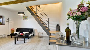 A modern living room with a black sofa, a wooden coffee table, a staircase with a metal railing, and a vase with flowers on a counter. - Nice home in Breznicki Hum with WiFi (Breznicki Hum)
