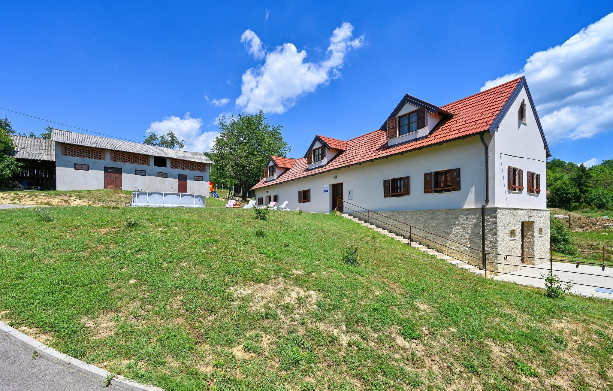 Une maison à deux étages, avec un toit recouvert de tuiles rouges, des fondations en pierre et une colline verdoyante.