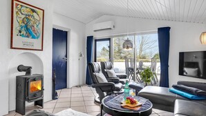 A modern living room with a fireplace, comfortable seating, a television, and a large window offering a view of the outdoors. - Amazing home in Juelsminde with sauna (Juelsminde)
