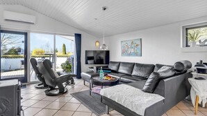 A modern living room with a grey leather sofa, a dining table, and a TV. - Amazing home in Juelsminde with sauna (Juelsminde)