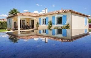 A two-story house with a tiled roof, blue shutters, and a pool reflecting the building. - Gorgeous home in Puisserguier (Puisserguier)