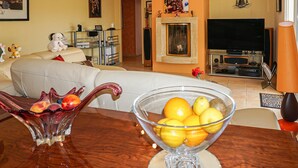 Un salon avec un canapé, une table en verre sur laquelle se trouve un panier de fruits, une cheminée et un téléviseur.