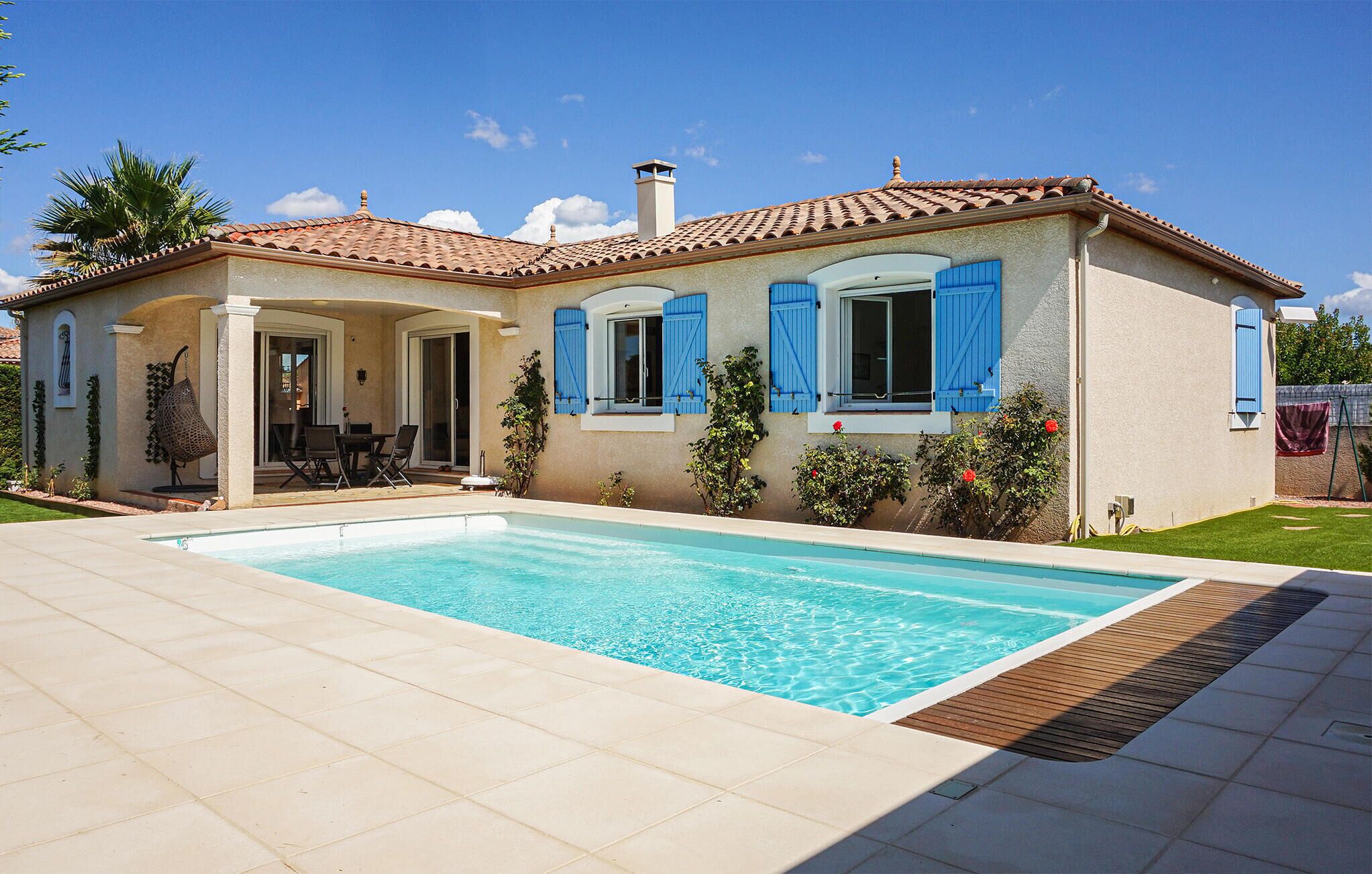 Una casa con piscina, un patio con mobiliario exterior y un jardín.