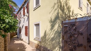 A narrow alleyway with a stone wall on one side and a building with shutters and a metal gate on the other.