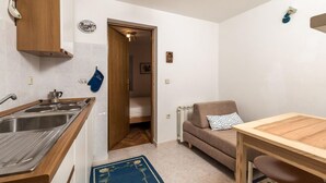 A compact kitchen with a wooden countertop, a sink, and a stove. There's a blue oven mitt on the wall and a small wooden cabinet above the sink.