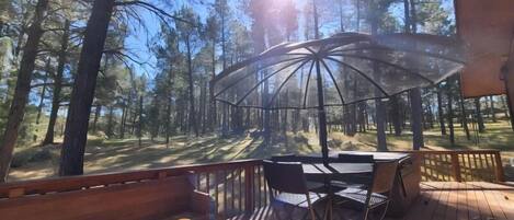 A deck with a table and chairs, surrounded by a forest.