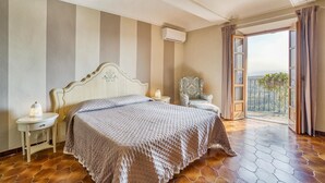 Une chambre avec un lit, des tables de chevet, une chaise et un balcon avec vue.