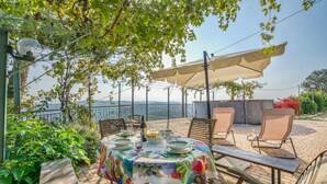 Un espace de restauration en plein air avec une table dressée pour deux personnes, entourée de chaises, et une pergola au-dessus.