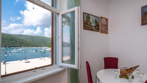 Una habitación con vista a un puerto deportivo, una mesa de comedor con una cesta y vasos, y dos cuadros en la pared.