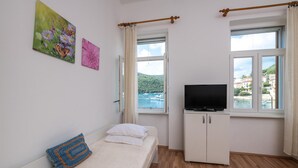Una habitación con una cama, un televisor sobre un mueble, y dos ventanas con cortinas.