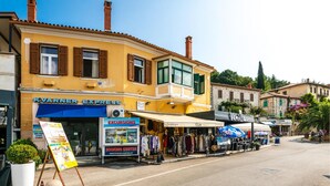 Una calle con un edificio amarillo que alberga una tienda KVARNER EXPRESS, una boutique llamada ELLA y una tienda Vanilla.
