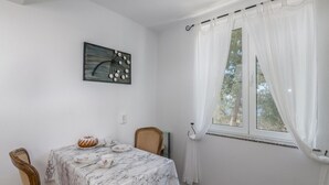 Un comedor con una mesa lista para cuatro, un cuadro en la pared y una ventana con cortinas traslúcidas.