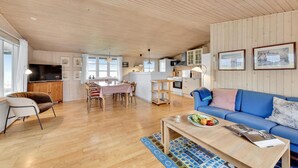 Un vaste espace de vie doté d’un plafond en bois, d’une table à manger, d’un canapé bleu et d’une cuisine à l’arrière-plan.