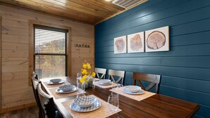 Une salle à manger avec une table en bois dressée pour six personnes, des assiettes à carreaux bleus et blancs, et un vase rempli de fleurs jaunes.