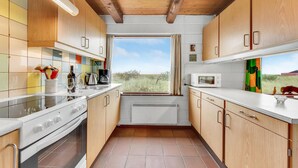 A compact kitchen with wooden cabinets, a white stove, and a window with a view of the outdoors.