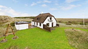 A white house with a thatched roof, a small attached shed, and a grassy yard.