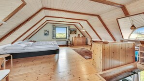 A cozy attic bedroom with a wooden ceiling, a bed, a dresser, and a window with a view of the outdoors.