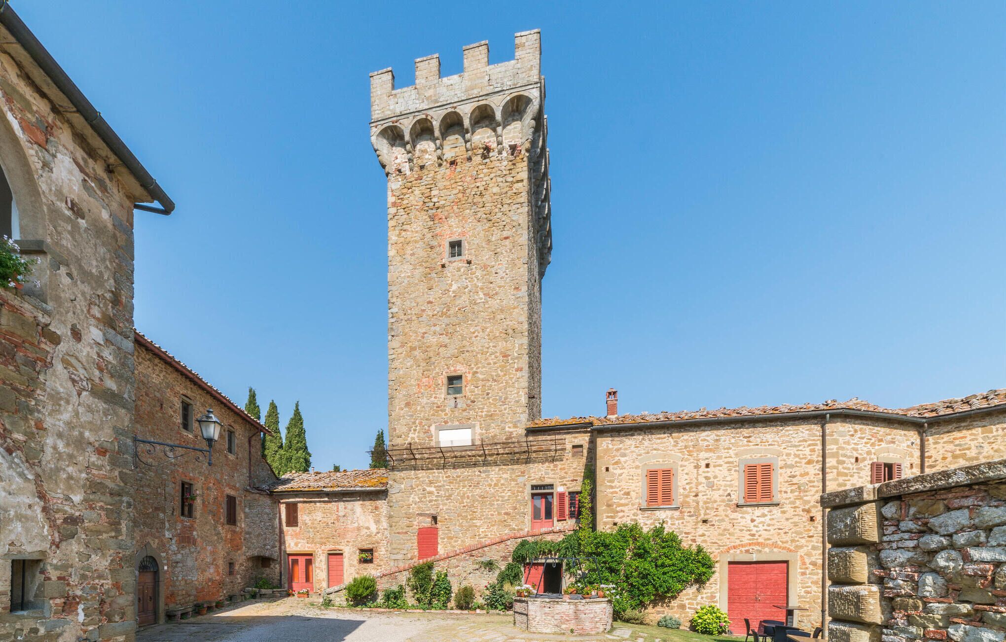 A historic stone tower with a crenellated top, adjacent buildings with red shutters, and a cobblestone courtyard.