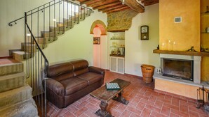 Un salon avec un canapé en cuir marron, une table basse en bois, une cheminée, une arche en pierre et un escalier avec des rampes en métal.