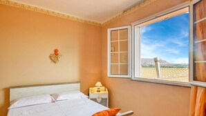 Een slaapkamer met een bed, een nachtkastje, een decoratief hart aan de muur en een raam met uitzicht op een verafgelegen landschap.