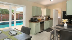 A modern kitchen with green cabinets, a dishwasher, and a coffee maker. There is a dining area with a table set for two. - Pool, Hot tub, Fire Pit, BBQ ~  Beautiful home with patio living at it's best! (Cottonwood)