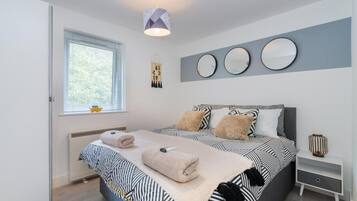 A modern bedroom with a large bed, a bedside table, a wall-mounted mirror, and a hanging decoration.
