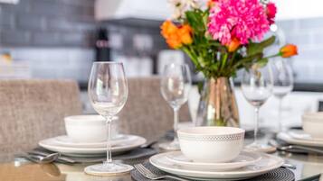 A dining table set with white plates, bowls, and wine glasses, accompanied by a vase of colorful flowers.