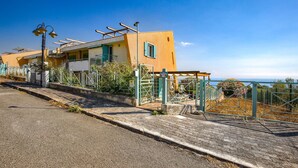 Un edificio sul lungomare con una strada pavimentata, cancelli in metallo e vista libera sul mare.