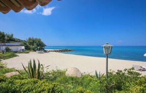 Una spiaggia con cielo azzurro intenso, un edificio bianco con tetto in tegole e un lampione.