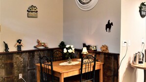 A cozy room with a wooden dining table, two chairs, a blue quilted bed, a wall clock, and a small shelf with decorative items. - Deluxe Single Queen Suite Futon & Kitchenette (Salmon)
