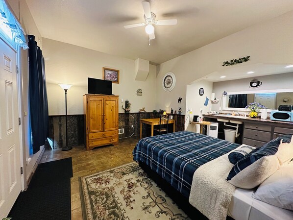A compact room with a bed, a desk, a kitchenette, and a wardrobe.