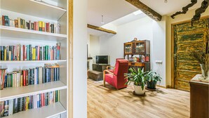 Una sala de estar con piso de madera, un sillón rojo, un televisor y una estantería llena de libros.