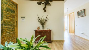 Un pasillo con suelo de madera, una puerta de madera pintada de verde, un armario de madera con un jarrón de plantas secas y una cruz en la pared.