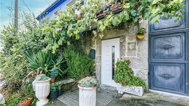 Un edificio de piedra con puerta azul, plantas en macetas y un pequeño jardín.