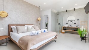 Una camera da letto moderna con un letto grande, comodini, TV integrata e bagno con specchio, lavabo e doccia.
