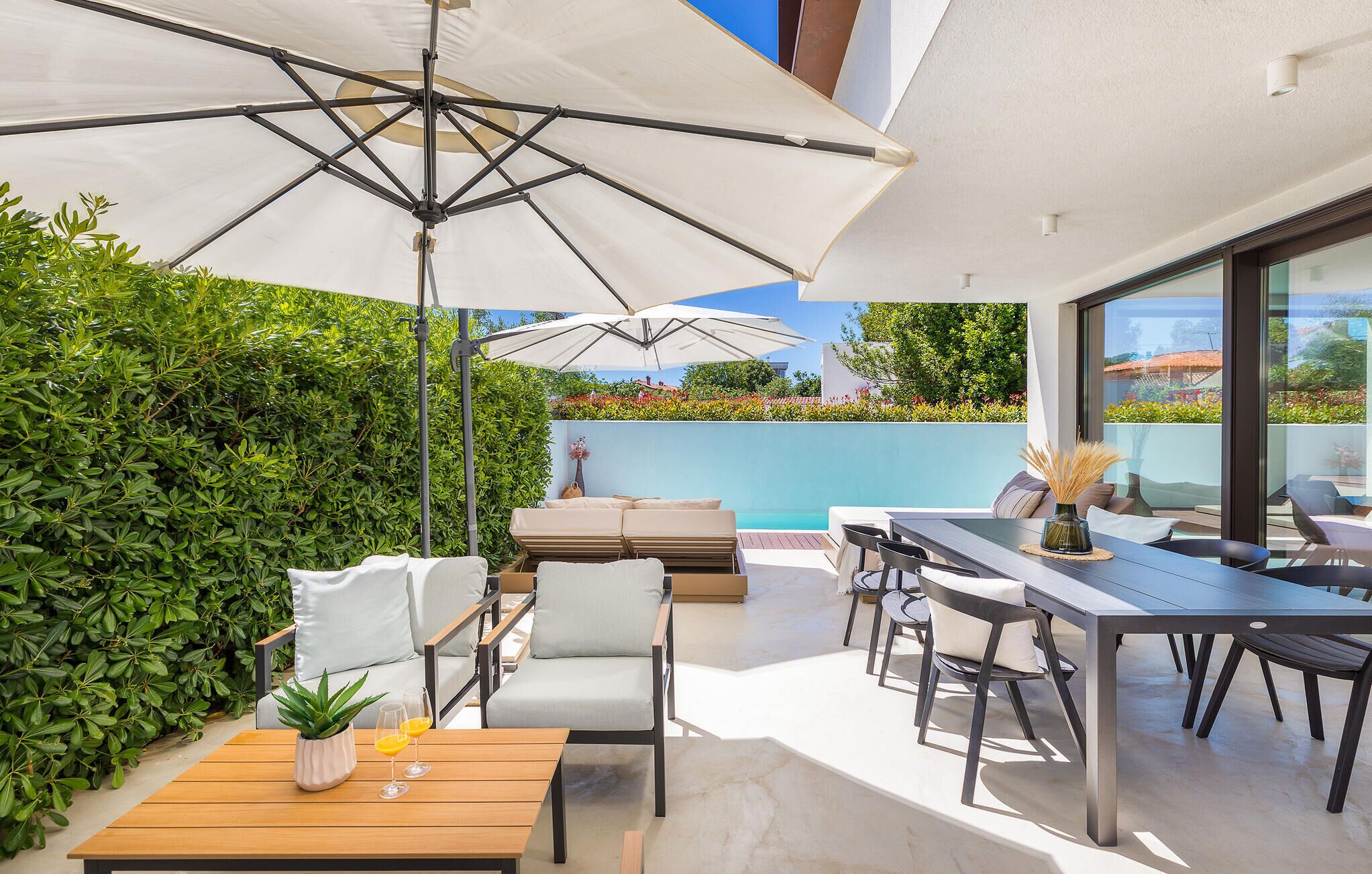 A modern outdoor patio with a pool, seating area, and umbrellas.