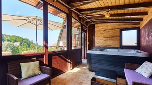 Una cabaña de madera con jacuzzi, mobiliario de mimbre y vistas del paisaje circundante.